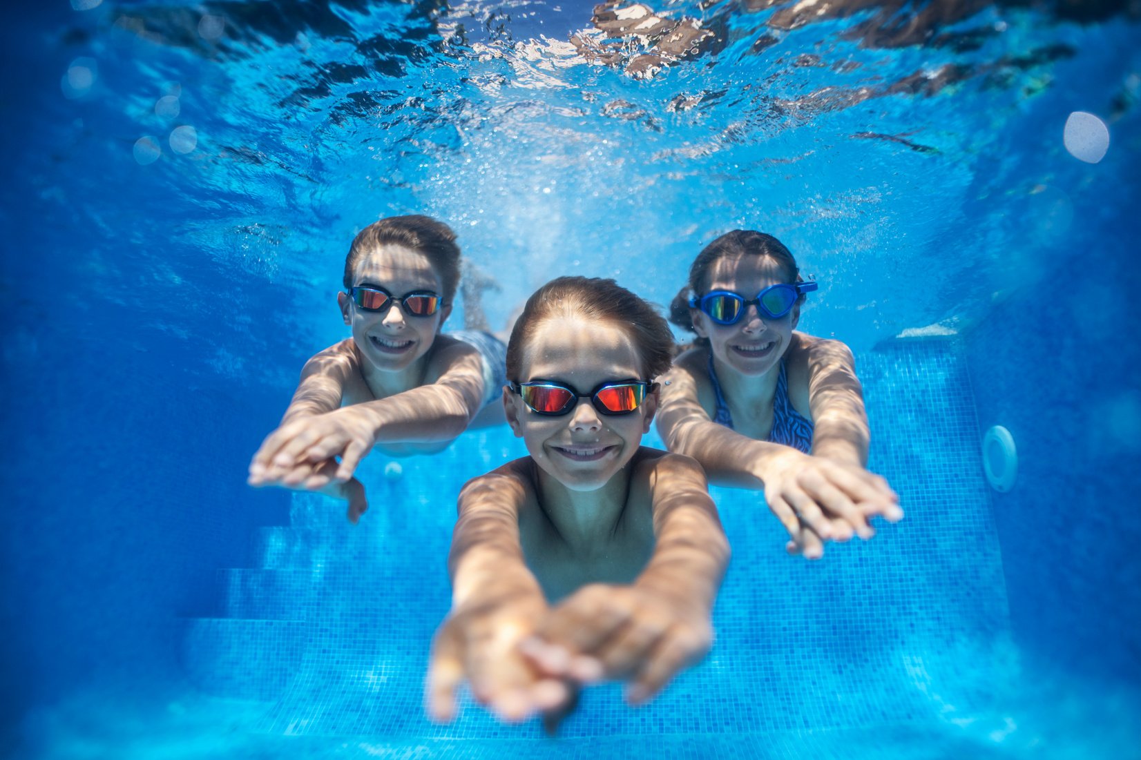 Three happy kids swimming underwater in pool